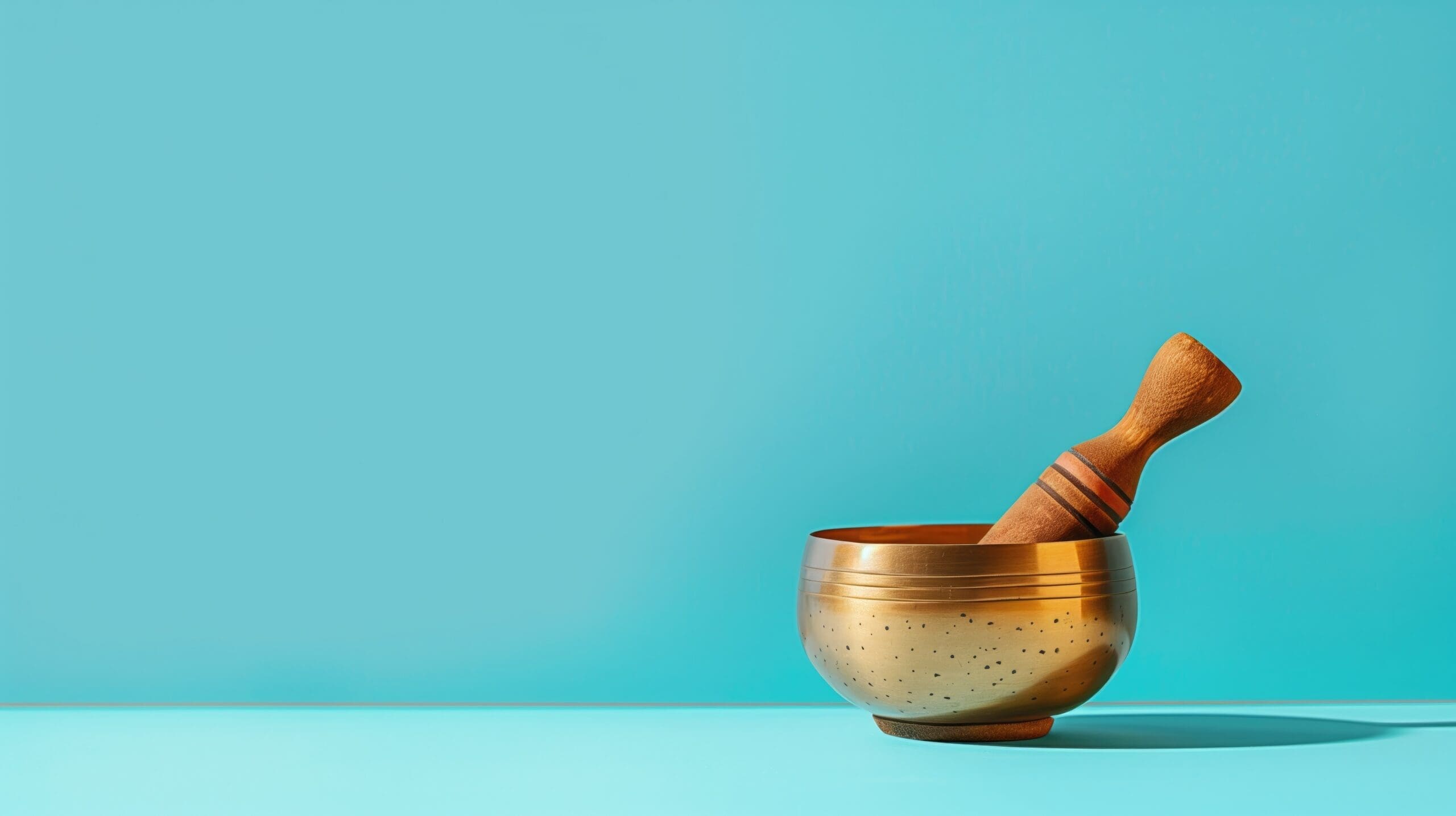 Singing bowl with a wooden mallet on a vibrant turquoise background