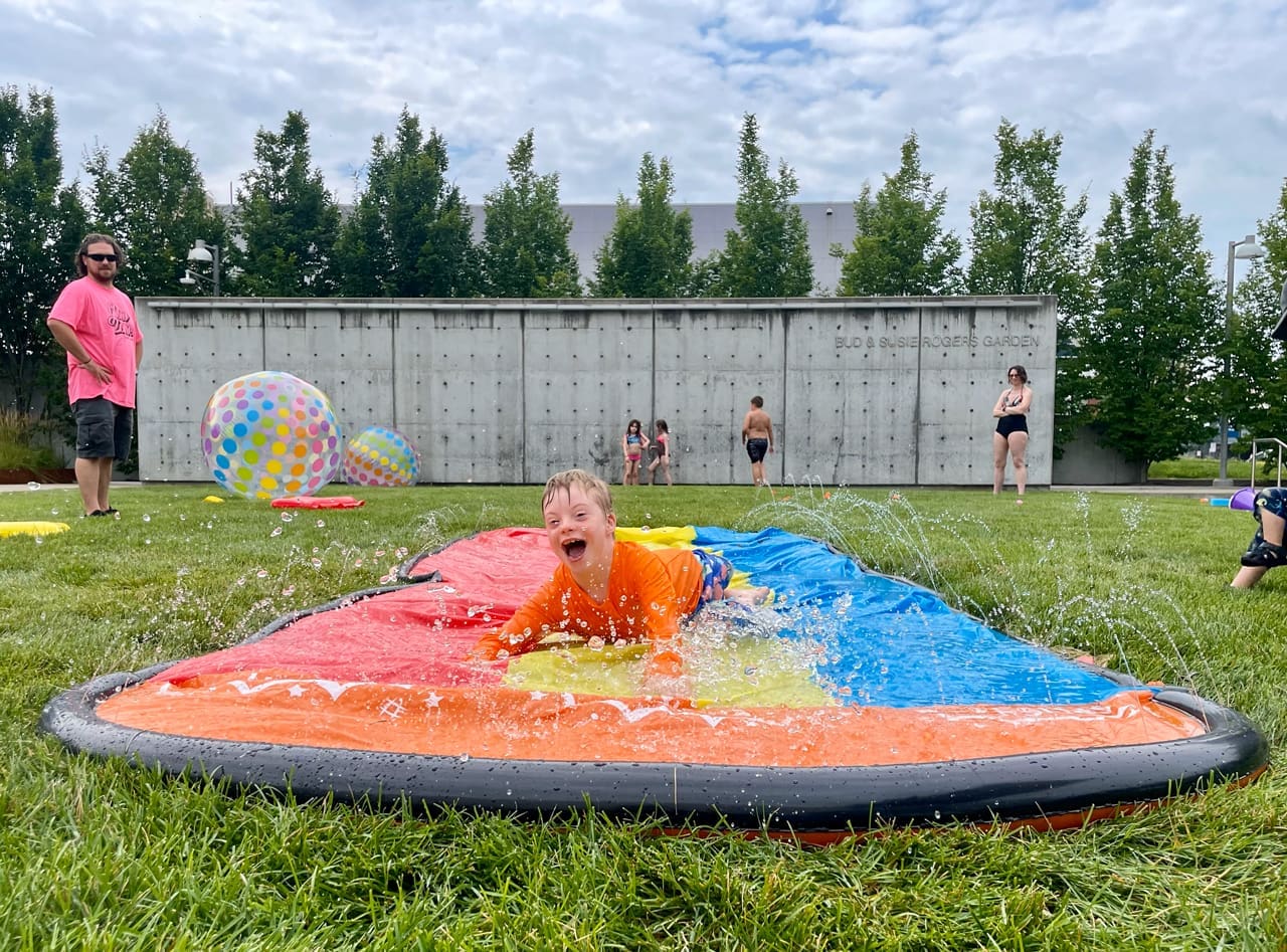 A kid sliding on a water slide in the garden at the Akron Art Museum